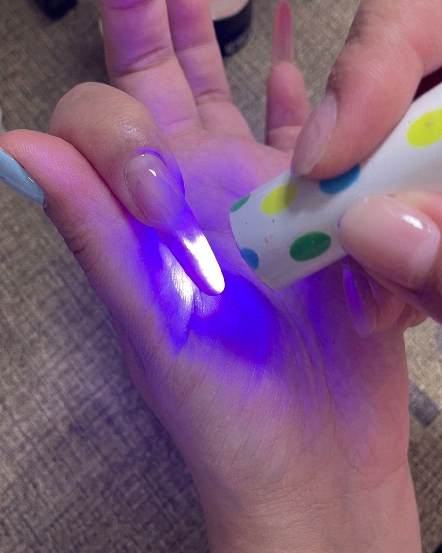 Une main tenant une lampe UV portable directement au-dessus des ongles pour catalyser la couche de gel finale.