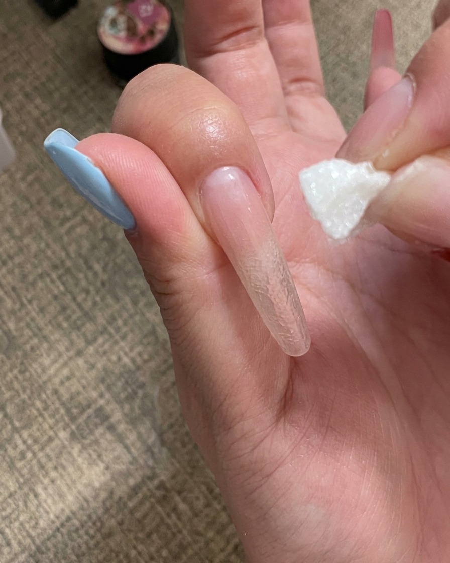 Une main plaçant un ongle sous une mini lampe UV portable.