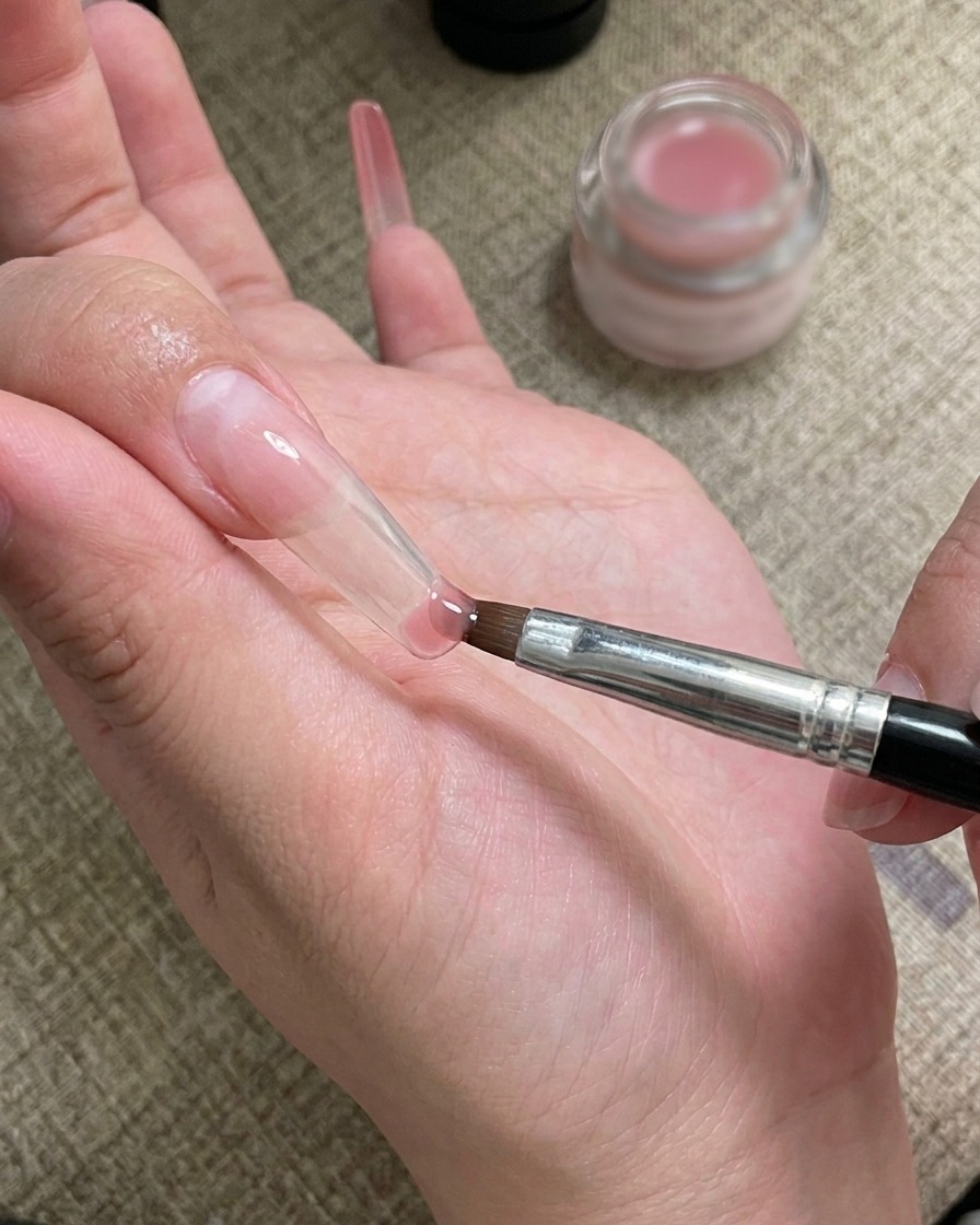 Un pinceau nail art appliquant et fondant du gel sur la pointe de longle.