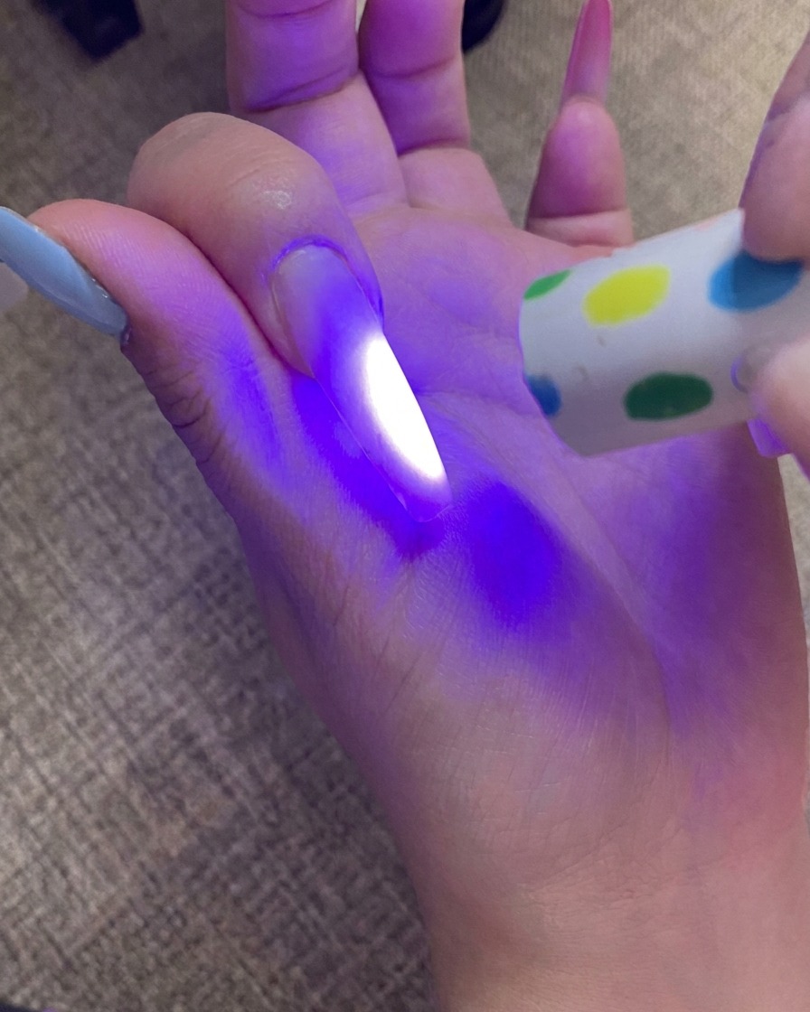 Une main catalysant longle avec pointe ombré sous une lampe UV, avec la lumière illuminant longle.