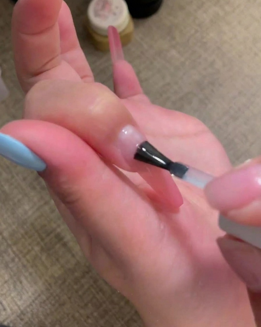 Un pinceau appliquant une base coat transparente et brillante sur la surface de longle.