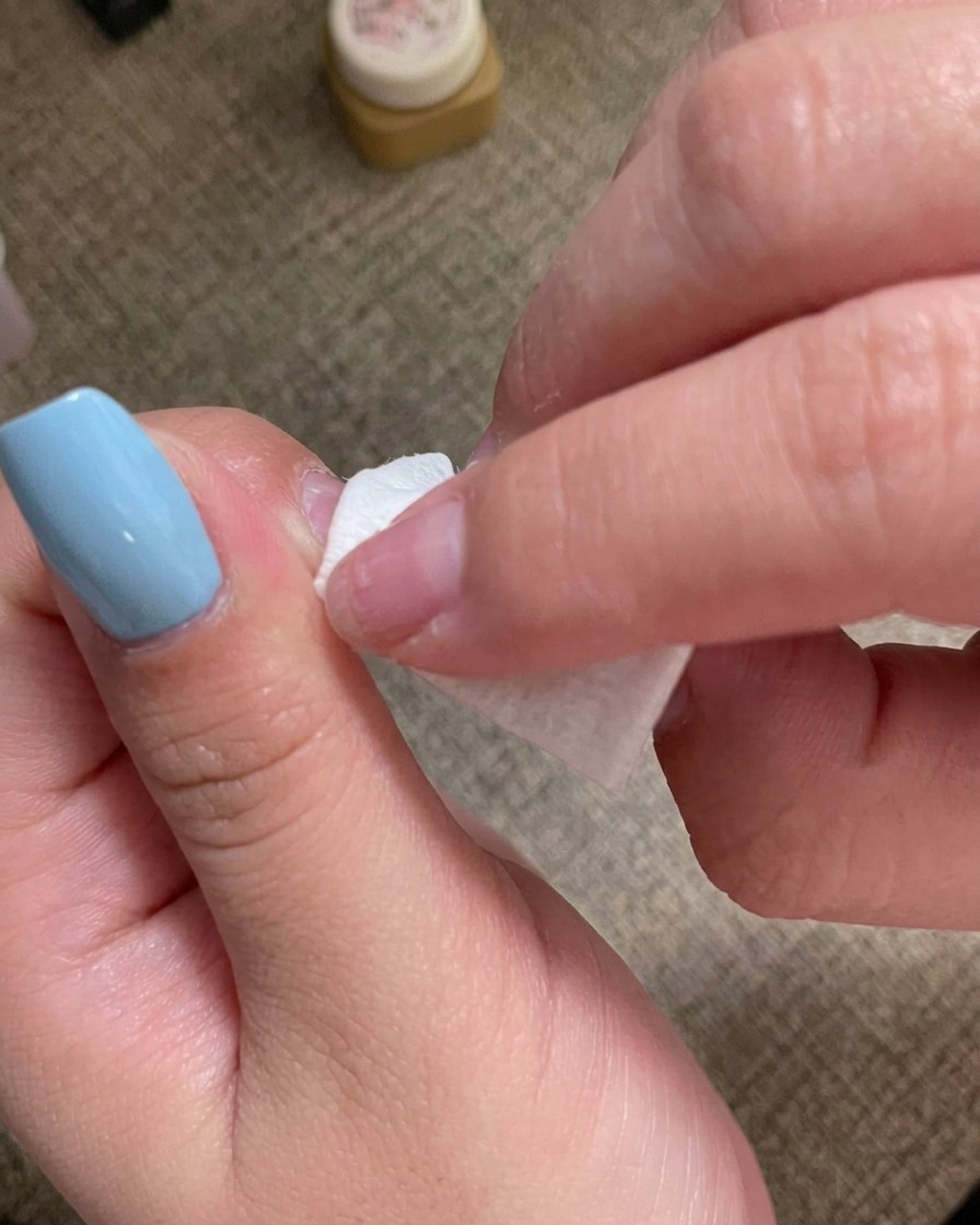 Une main utilisant une lingette non pelucheuse pour nettoyer la surface dun ongle manucuré.