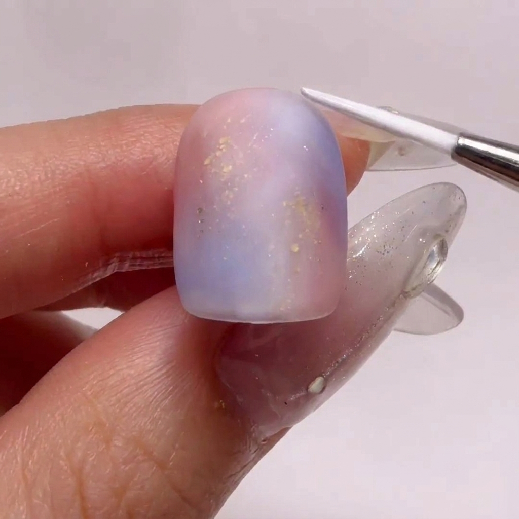 Un pinceau fin créant des motifs dondulations blanches sur un ongle au fini mat.
