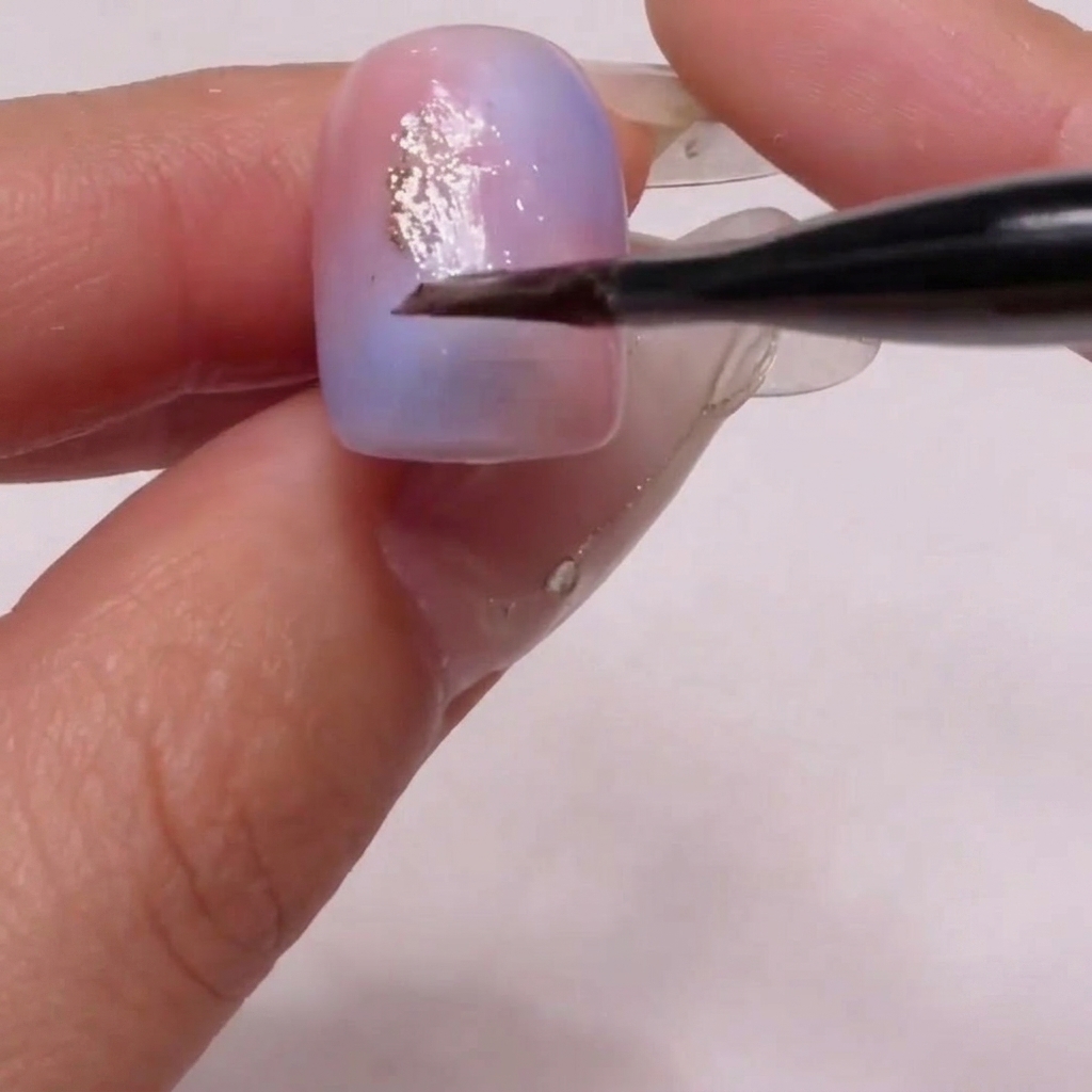 Un pinceau déposant délicatement des particules de paillettes dorées sur la surface de longle.