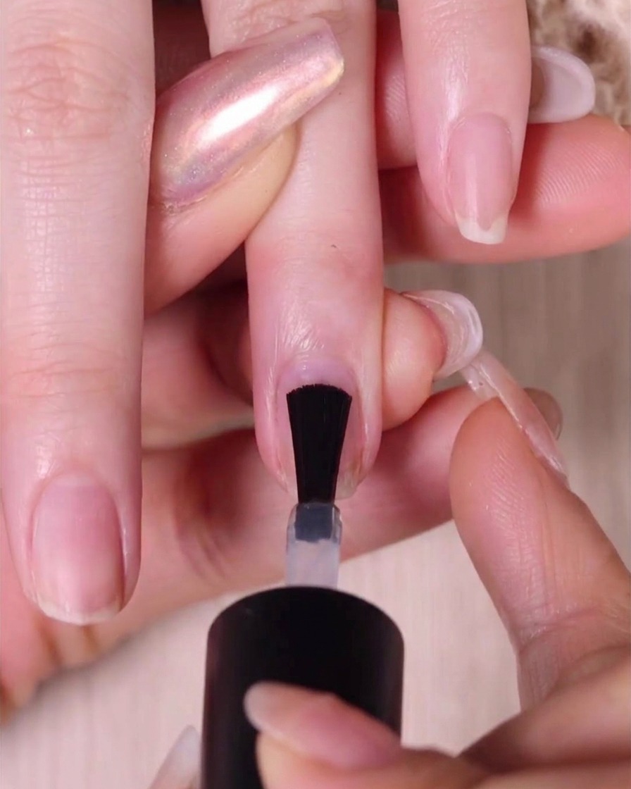 Gros plan dun pinceau à vernis appliquant une base transparente sur un ongle naturel nu.