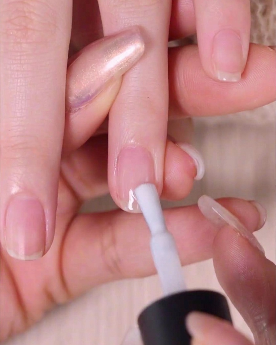 Gros plan dune main utilisant un pinceau pour appliquer une fine couche de vernis blanc transparent sur un ongle naturel.