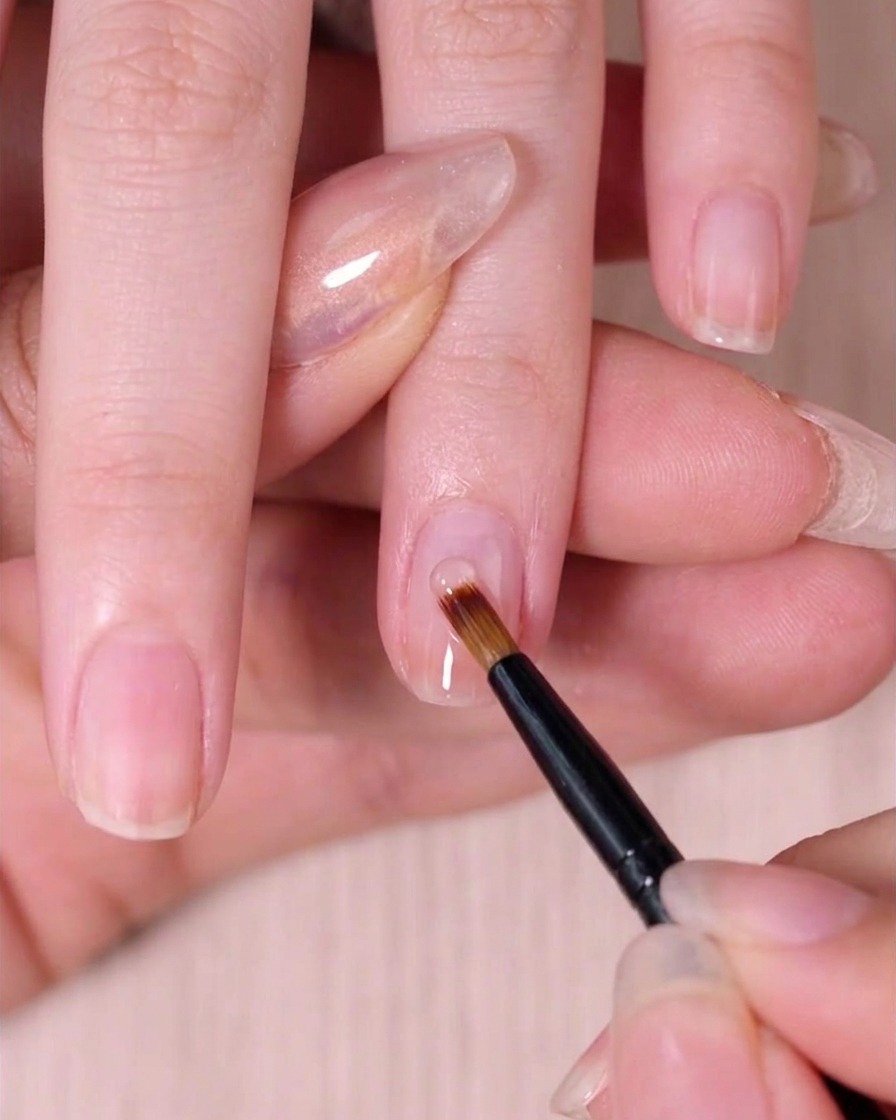 Un pinceau à ongles spécialisé pour lestompage mélangeant délicatement le vernis rose humide sur longle pour créer un effet ombré.