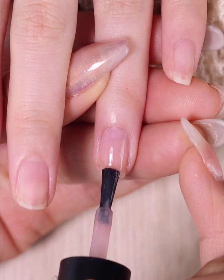 Un pinceau appliquant une deuxième couche de vernis rose nude sur la moitié supérieure de longle sur une couche précédemment estompée.