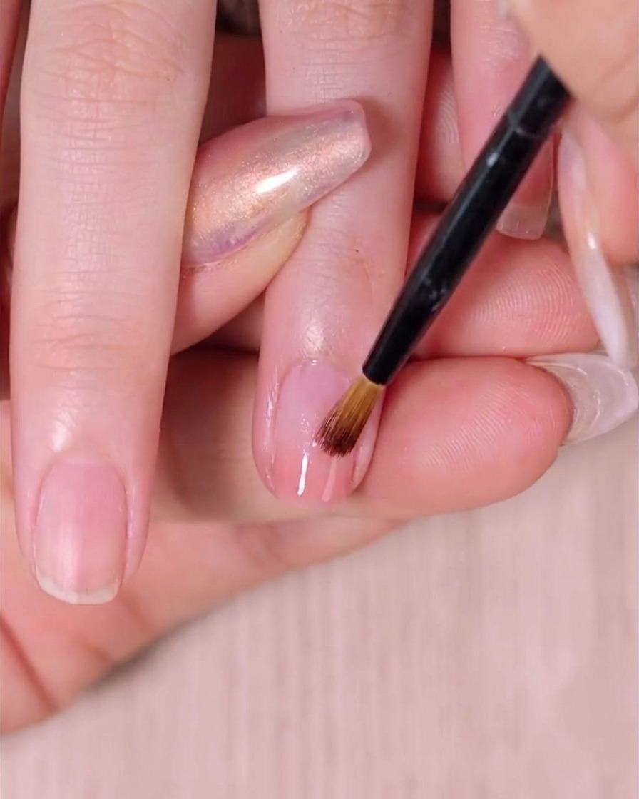 Un pinceau à ombré estompant doucement la deuxième couche de vernis rose pour parfaire le dégradé sur un ongle.