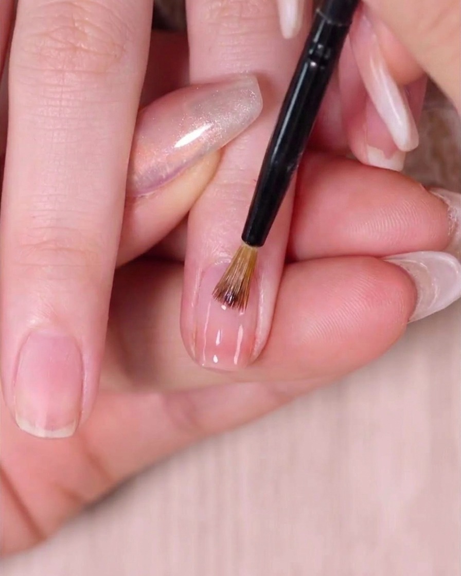 Un pinceau nail art fin estompant délicatement le vernis rose humide près de la cuticule pour créer un mélange sans démarcation.