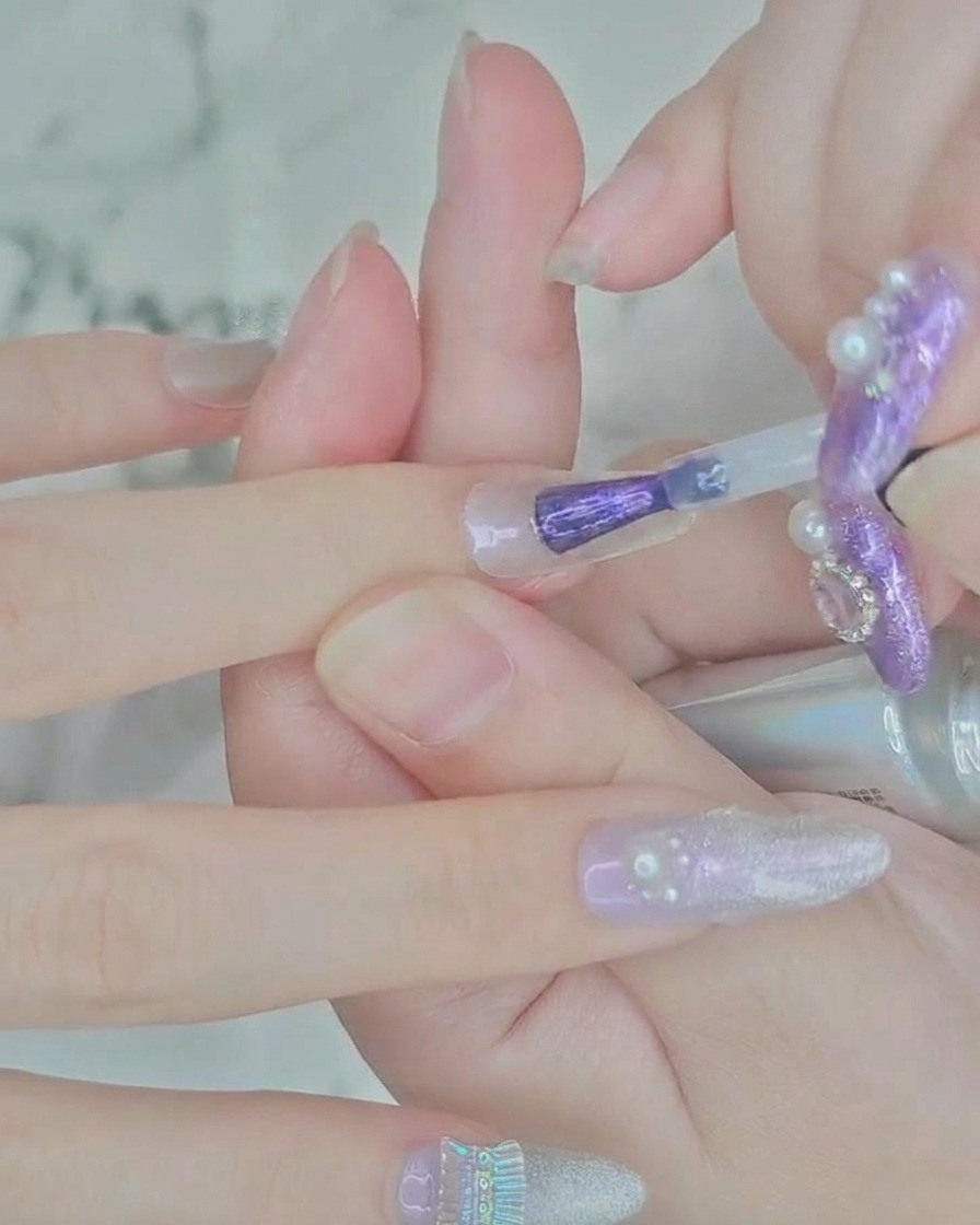 Gros plan dun pinceau appliquant du vernis gel violet translucide au centre dune extension dongle transparente.