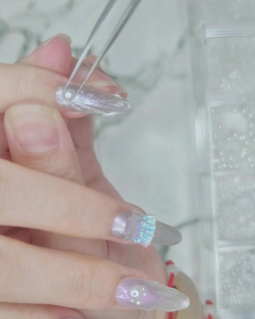 Une pince à épiler plaçant de petites perles blanches dans une ligne de gel transparent humide sur longle.