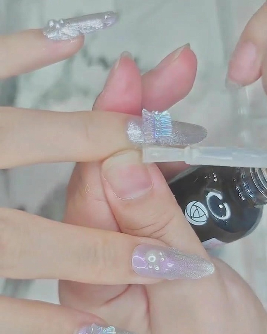 Un pinceau appliquant une couche de top coat transparent et brillant sur longle et les perles décoratives.