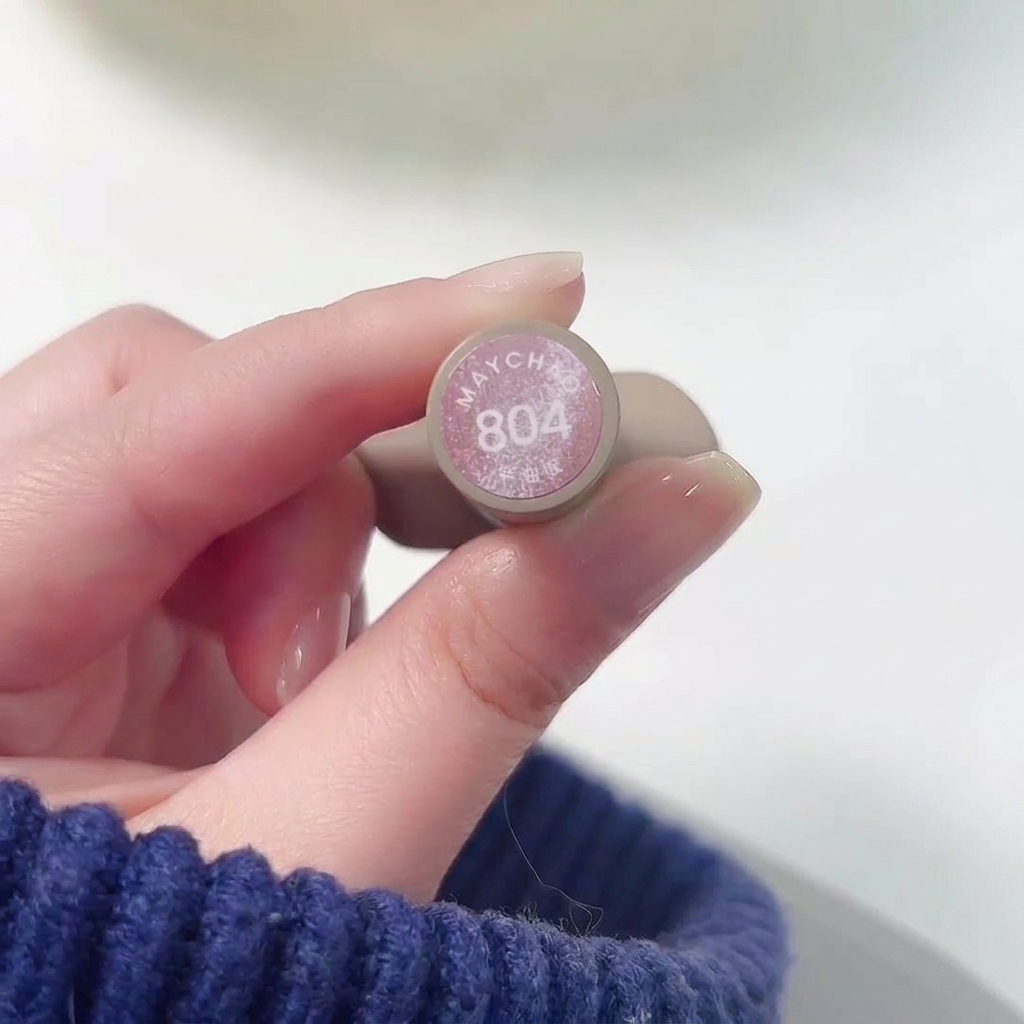 Gros plan dune main tenant le flacon de Meichao 804 Taozhi Yaoyao lors de lapplication du vernis rose nude scintillant sur un ongle.