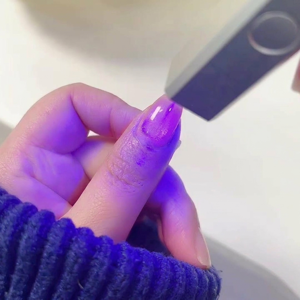 Un doigt avec du vernis gel violet humide et scintillant placé à lintérieur dune lampe à ongles UV/LED allumée.