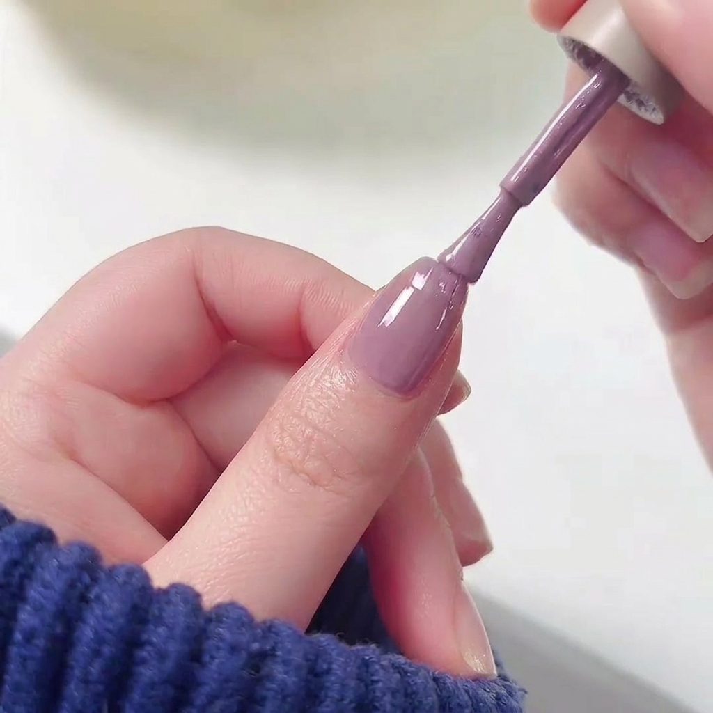Un pinceau de vernis à ongles appliquant du vernis gel violet sur la moitié supérieure dun ongle au-dessus dune base rose.