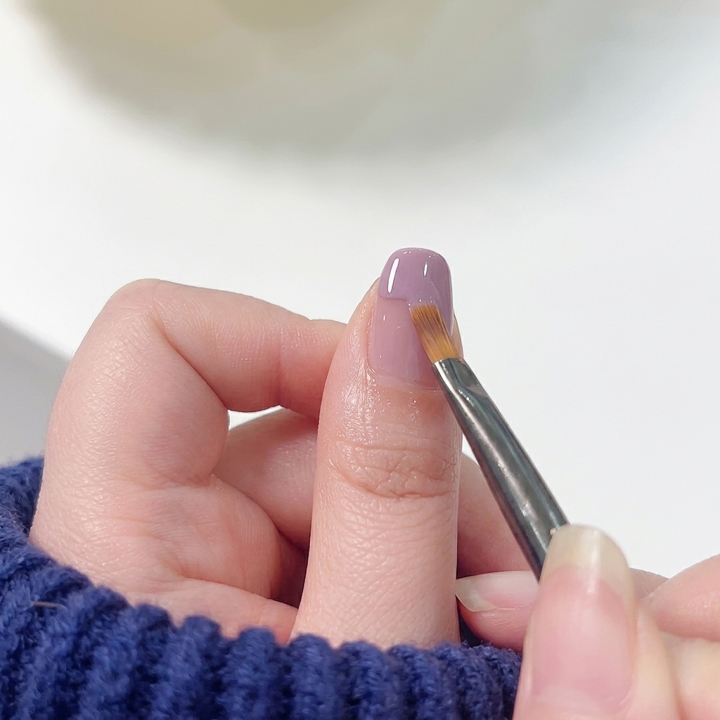 Un pinceau plat pour nail art balayant doucement le bord inférieur du vernis violet vers le bas dans une base rose pour créer un dégradé sans démarcation.