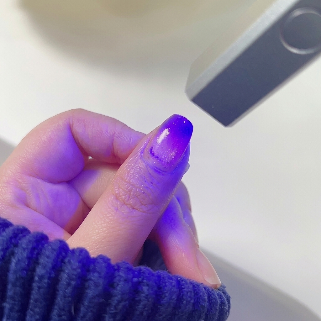 Longle du pouce avec un dégradé rose et violet fondu catalysant sous la lumière violette dune mini lampe à ongles LED.