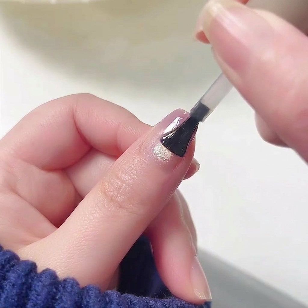 Un pinceau appliquant un top coat transparent et ultra-brillant sur la surface dun ongle qui présente déjà un motif de dégradé rose et violet fondu.
