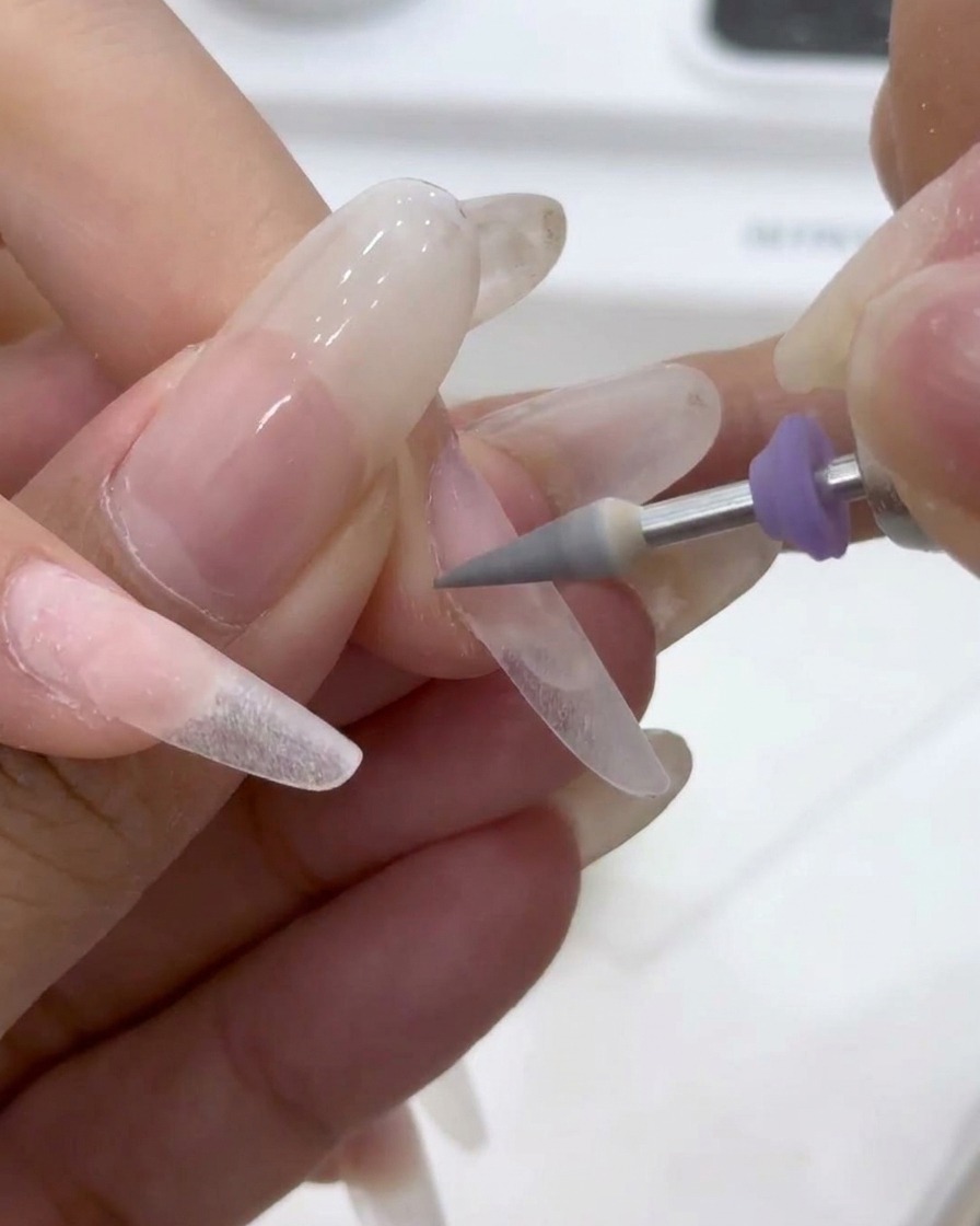 Un embout de ponceuse conique gris affinant les contours et la surface de longle.