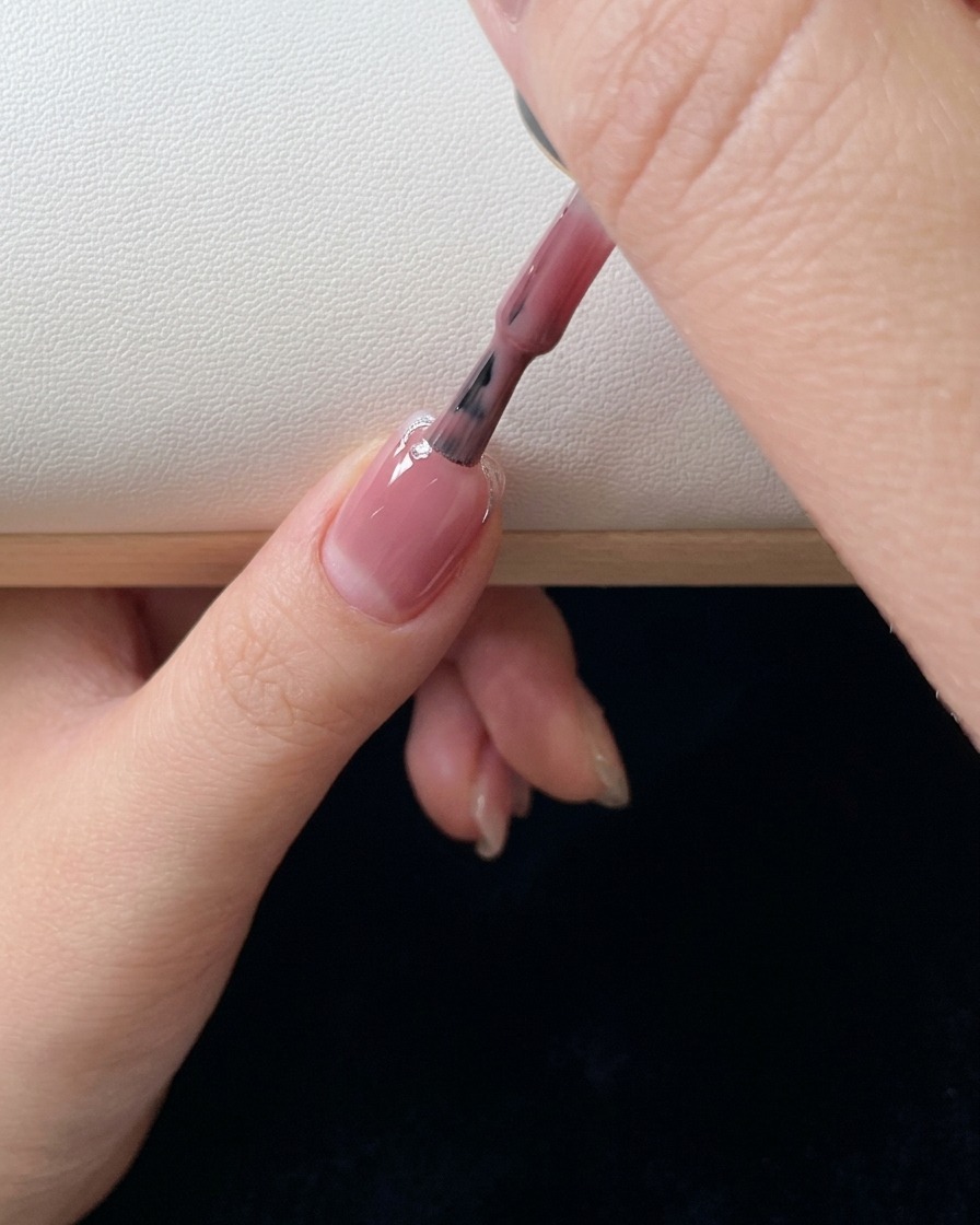 Gros plan sur un pinceau appliquant une seconde couche de gel rose et estompant la couleur sur longle.