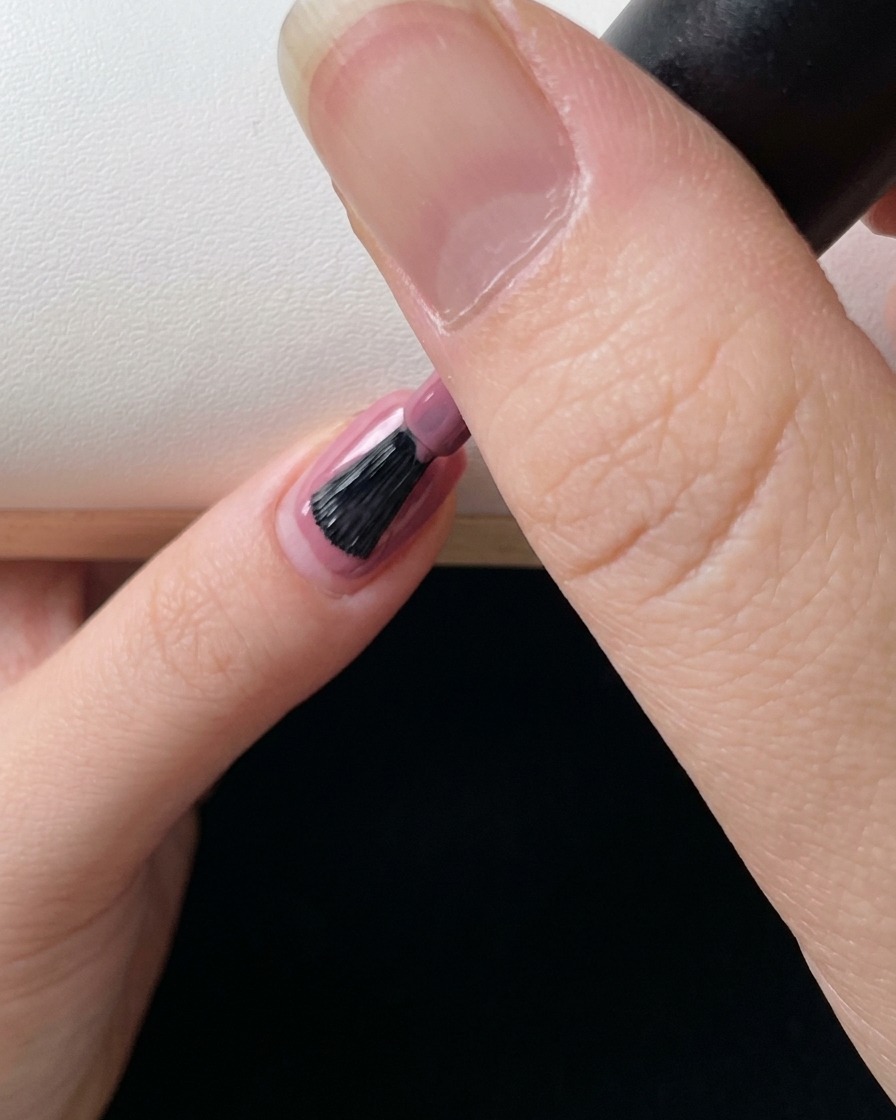 Gros plan sur un pinceau à ongles appliquant une couche finale de gel rose pour parfaire le dégradé.