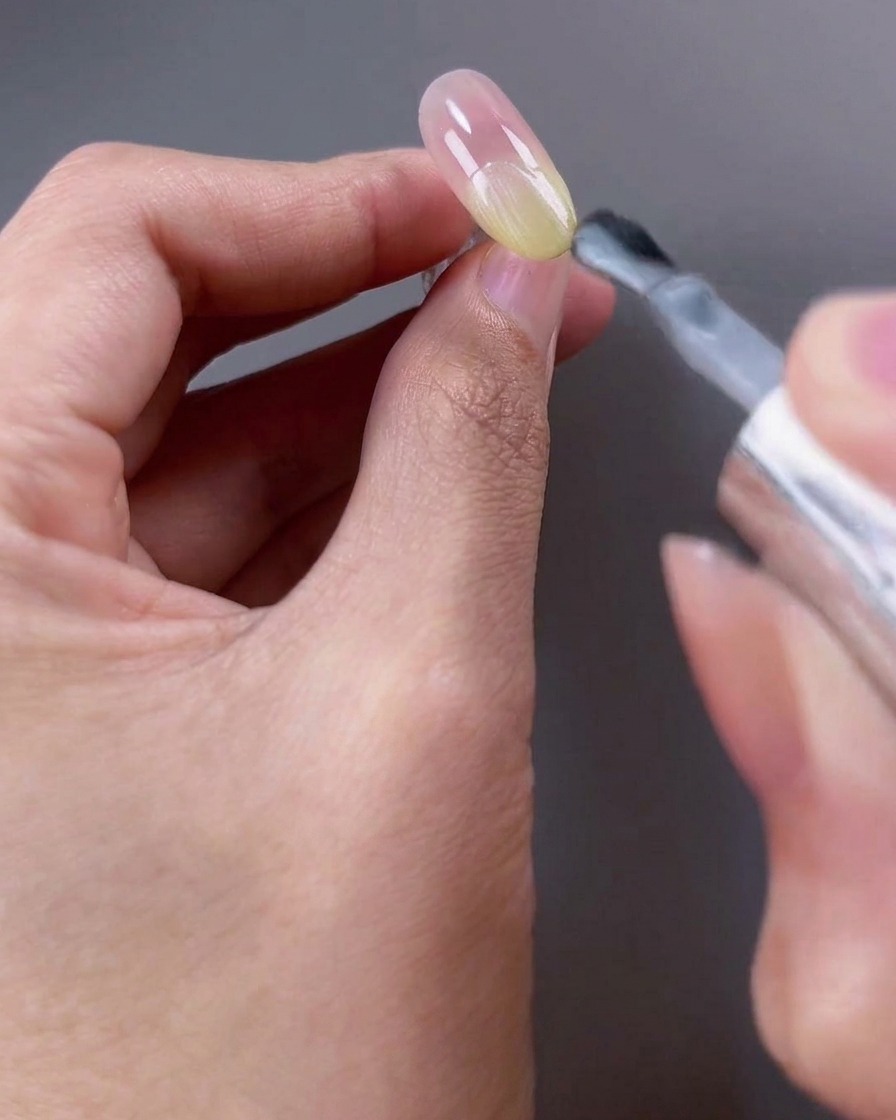 Pinceau appliquant un vernis gel blanc translucide scintillant sur la moitié supérieure de longle.