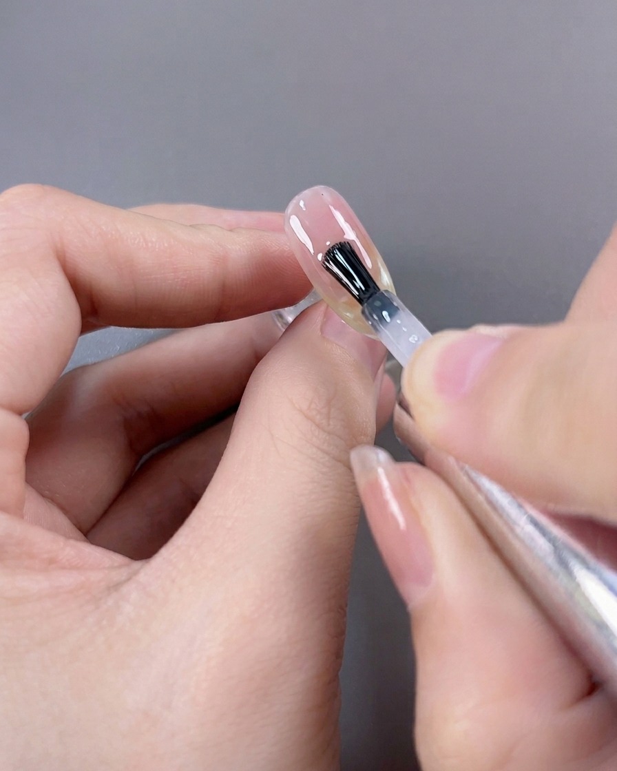 Pinceau appliquant une dernière couche de finition très brillante sur une manucure French cat-eye terminée.
