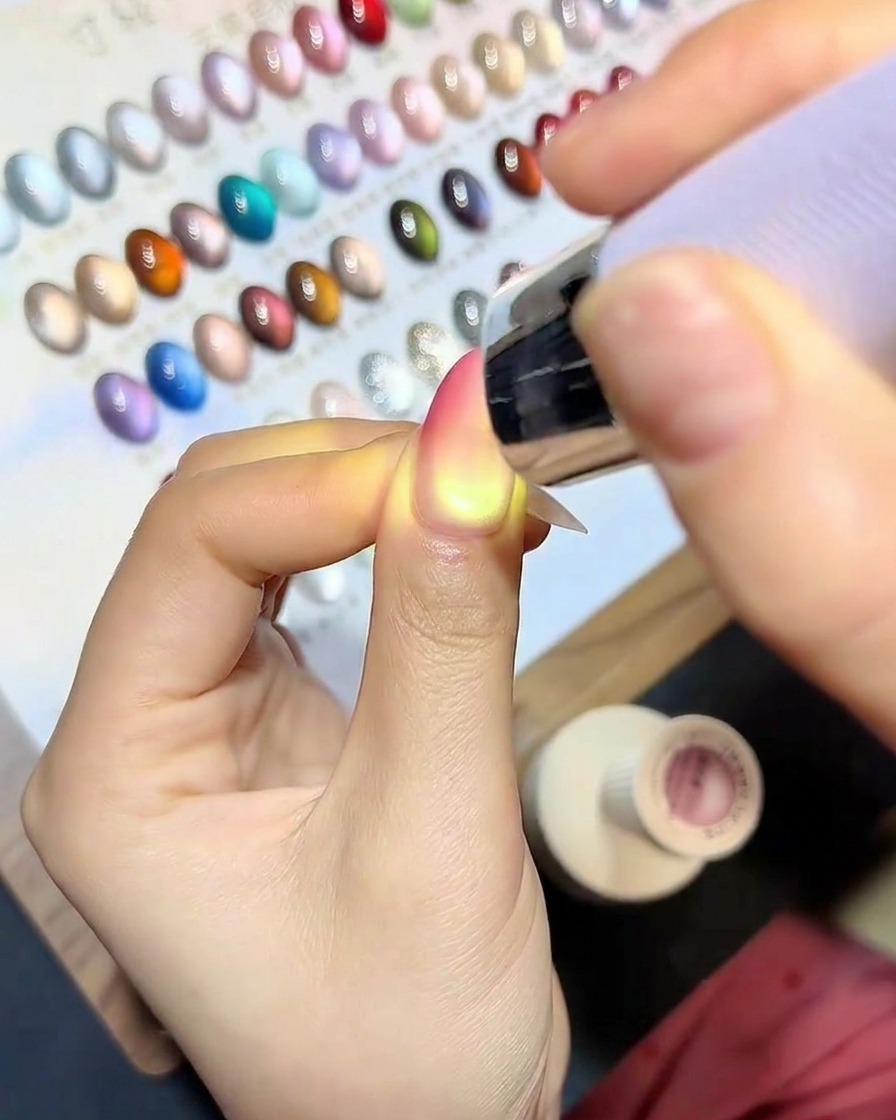Un pinceau appliquant un top coat transparent et brillant sur longle fini en dégradé œil de chat.