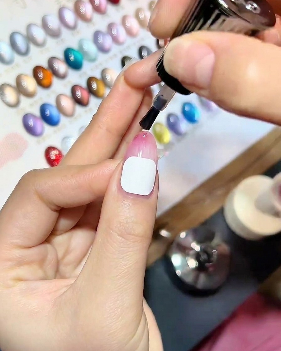 Gros plan dune main avec un top coat fraîchement appliqué reposant à lintérieur dune lampe à ongles UV professionnelle, avec une lumière bleue illuminant les ongles.