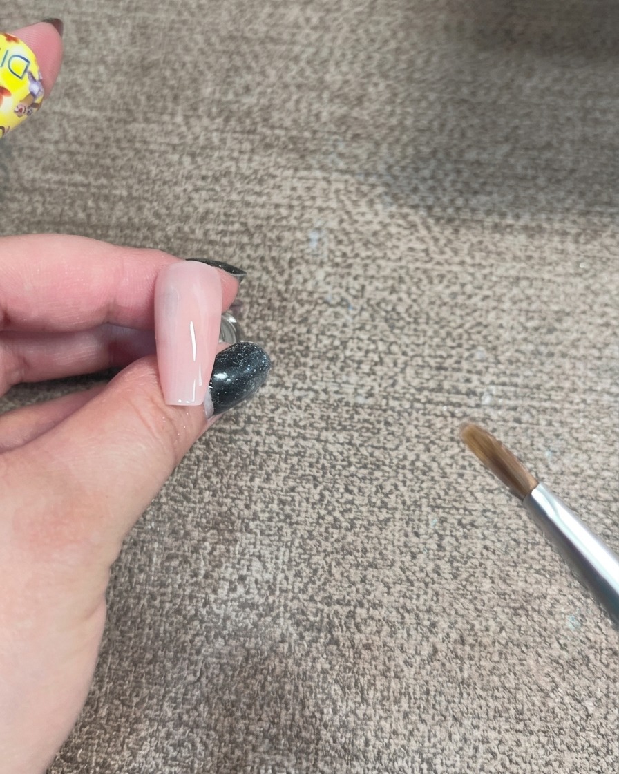 Gros plan dun pinceau appliquant un gel irisé en courbe sur une base dongle rose clair.