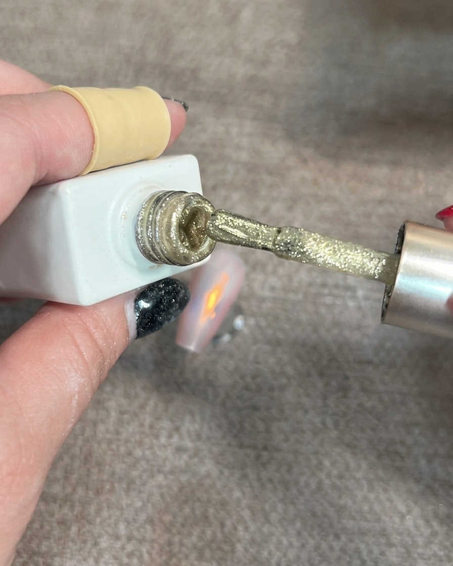 Pinceau appliquant de petites touches de gel cat-eye doré sur un ongle décoré.
