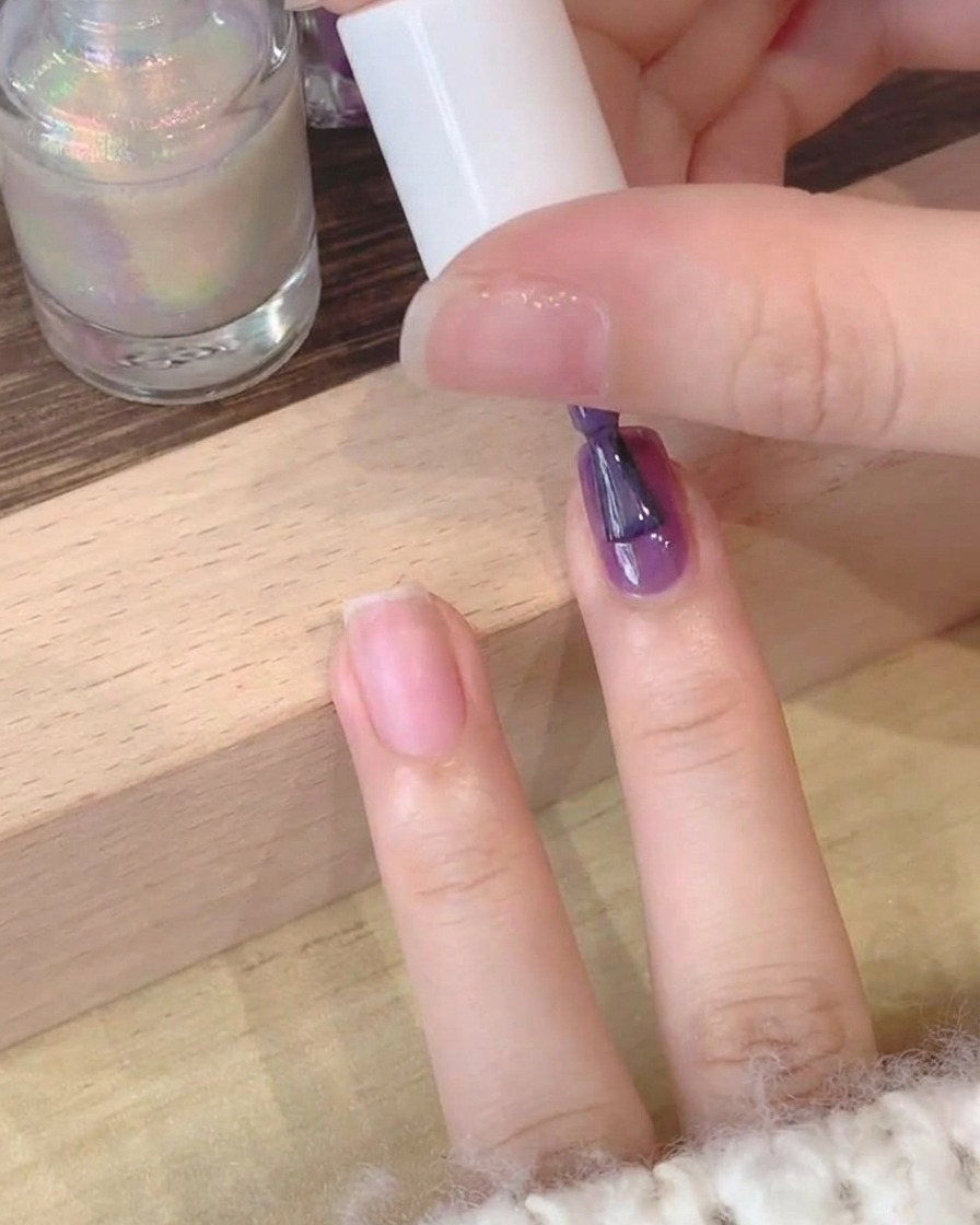 Gros plan dun pinceau appliquant du vernis gel violet profond sur un ongle naturel.