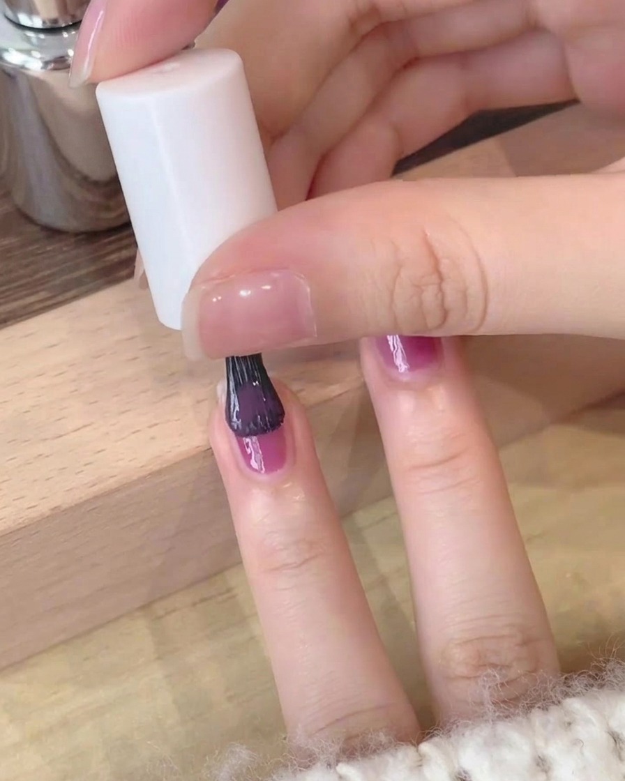 Gros plan dune seconde couche de vernis gel violet profond appliquée avec soin sur un ongle.
