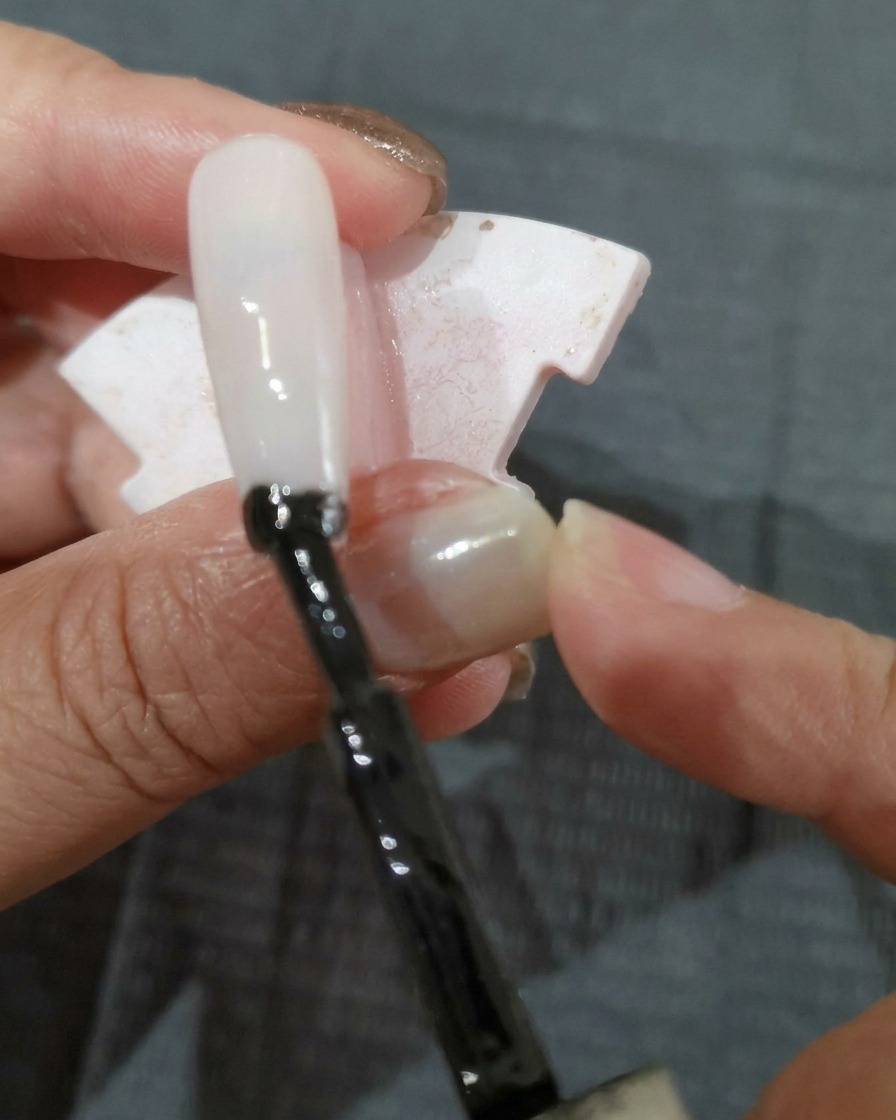Un pinceau appliquant une couche de vernis gel noir sur un ongle.