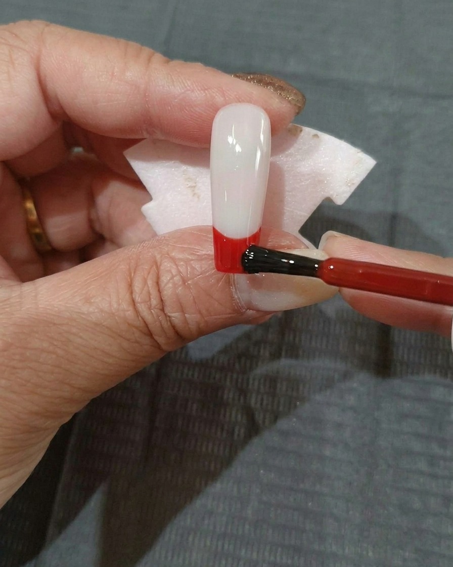 Une fine couche de vernis gel rouge appliquée sur la section inférieure dun ongle à base noire.
