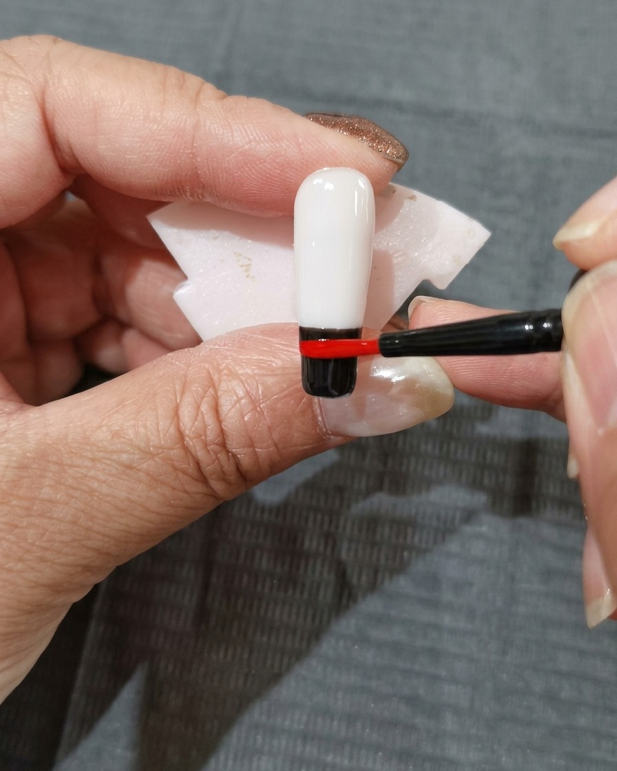 Une traînée de vernis gel rouge-orangé placée juste au-dessus de la bande rouge sur longle.