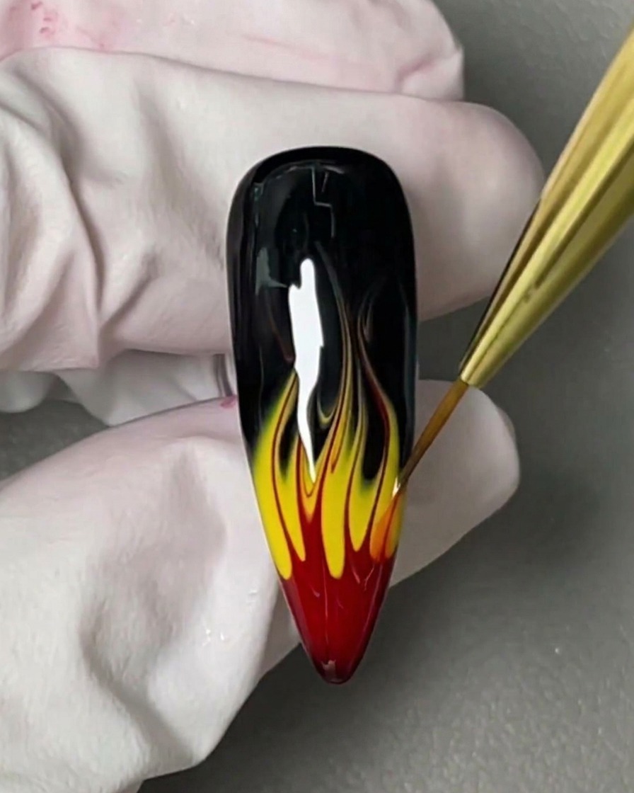 Un pinceau appliquant un blooming gel transparent sur un ongle noir brillant.
