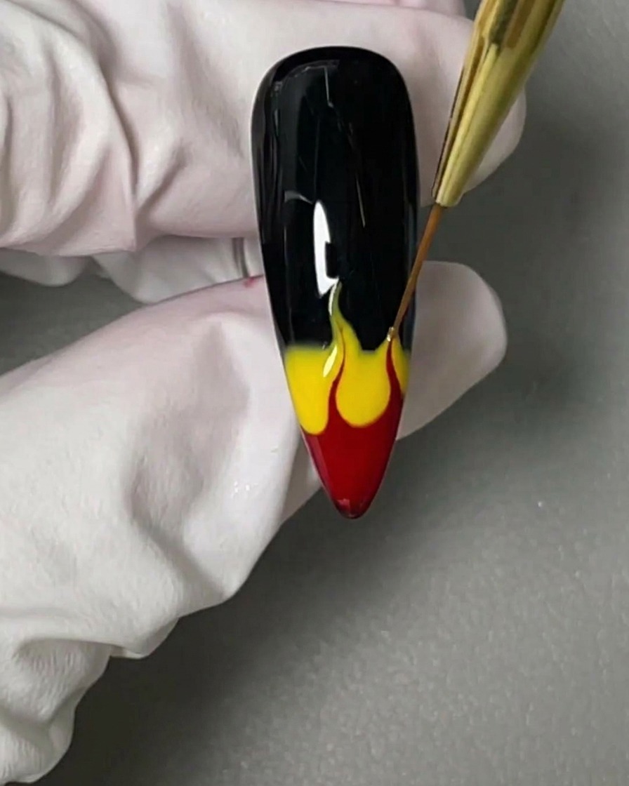 Un pinceau liner étirant les gels rouge et jaune vers le haut pour former des flammes.