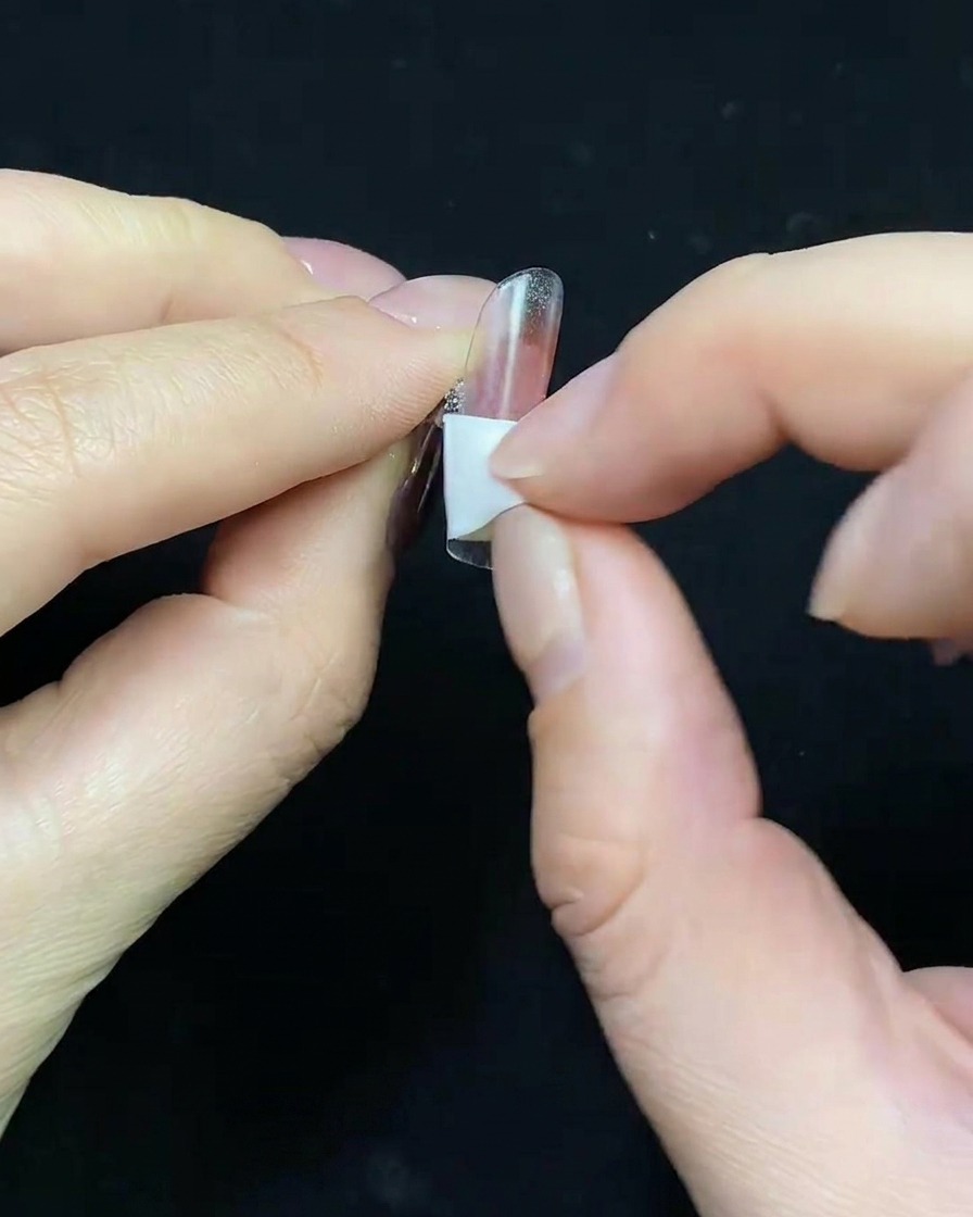 Gros plan sur un pinceau appliquant une base gel nude sur une capsule transparente.