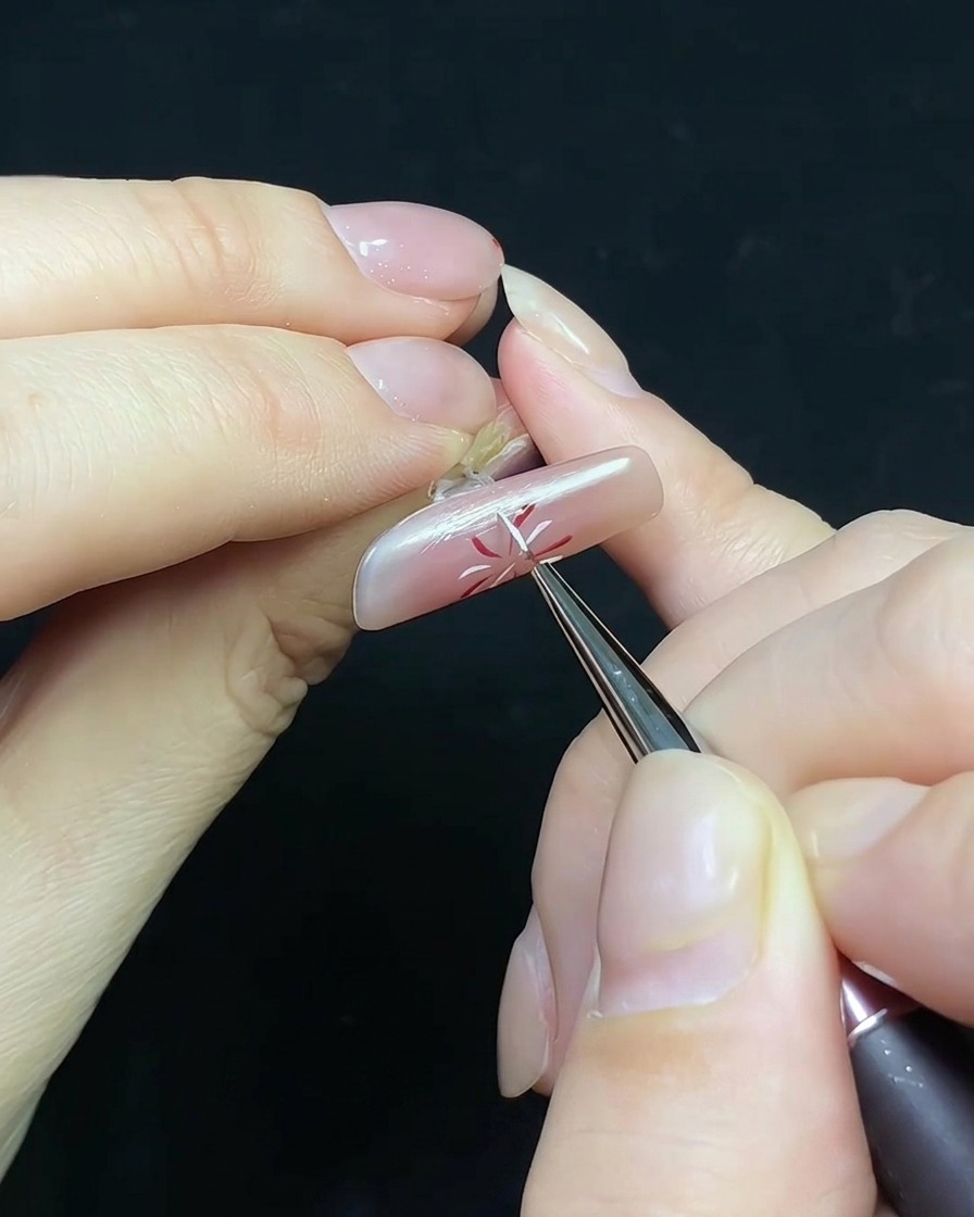 Un pinceau appliquant du top coat sur un ongle au design feu dartifice avec une petite perle décorative.