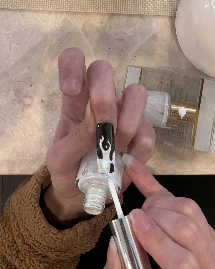 Un pinceau appliquant une fine couche de vernis blanc uniquement sur les zones de flammes.