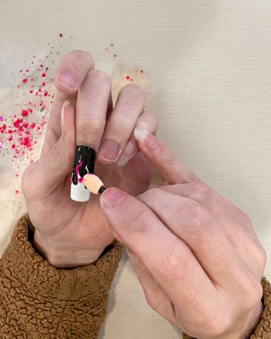 Un applicateur éponge tamponnant du pigment rose vibrant sur les détails de flammes blanches.