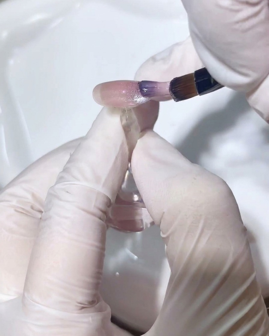 Un pinceau fin mélangeant délicatement le vernis cat-eye pour un dégradé fondu.