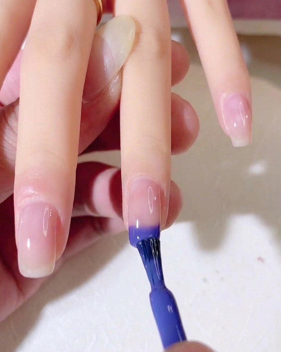 Un pinceau à ongles applique un dégradé de gel bleu et violet sur le bout dun ongle naturel.