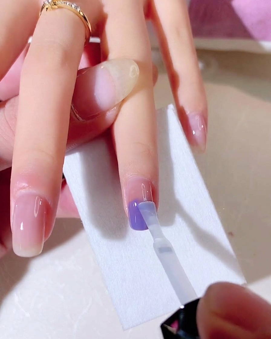 Un pinceau imbibé de base coat transparent est utilisé pour mélanger verticalement les couleurs bleu et violet sur longle.
