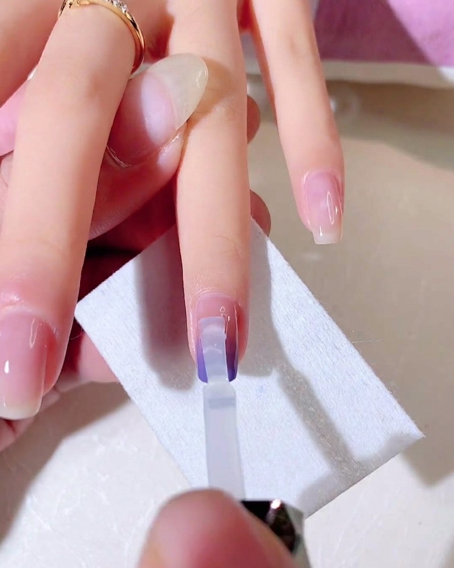 Un pinceau gel transparent mélange la seconde couche de couleur dégradée vers le bas de longle.
