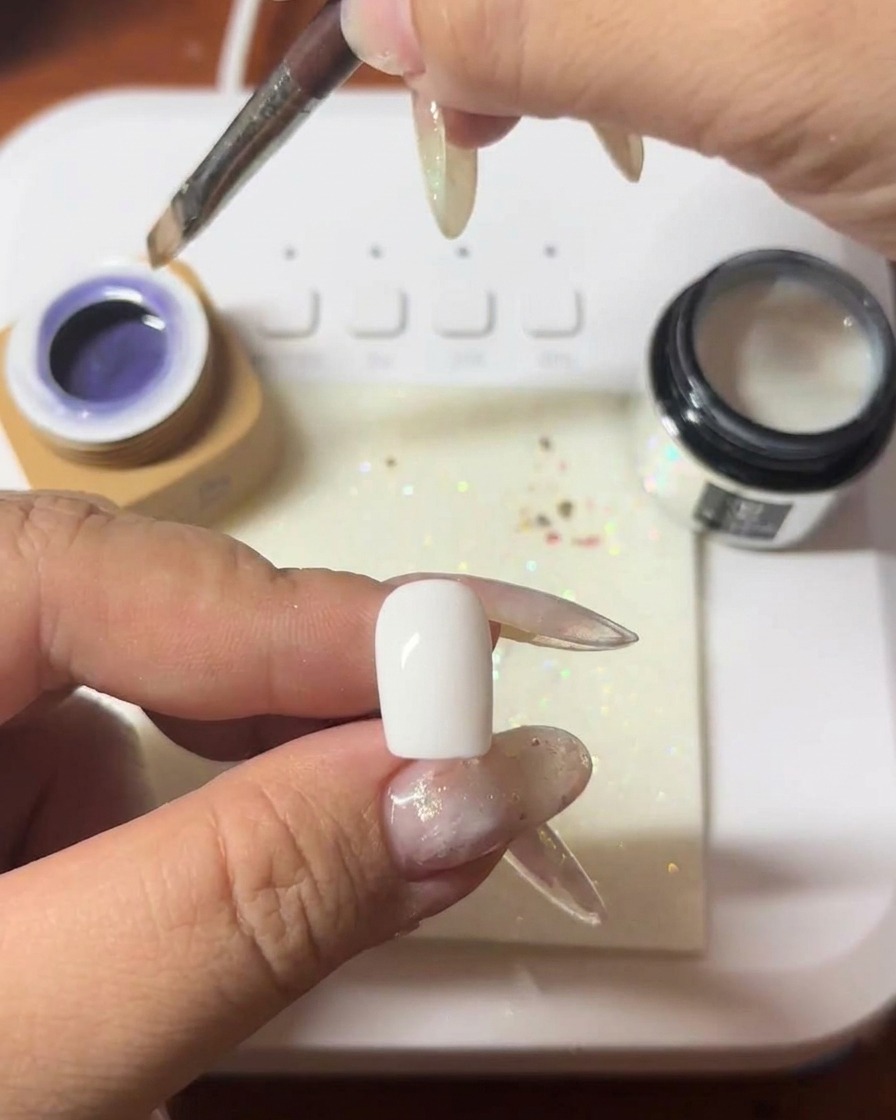 Un pinceau appliquant une couche de gel cat-eye violet profond sur un ongle.