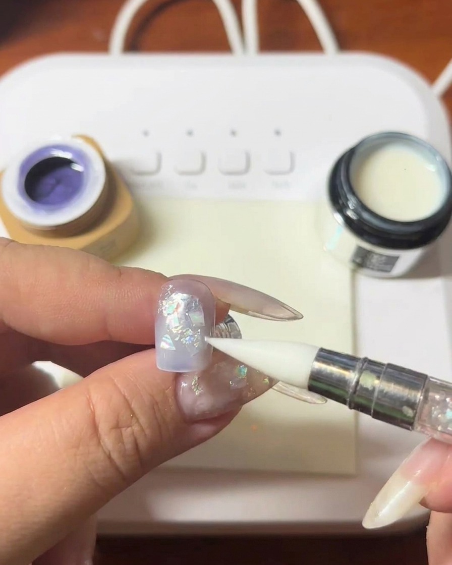 Un outil à embout silicone pressant sur des coquillages sur la surface dun ongle.