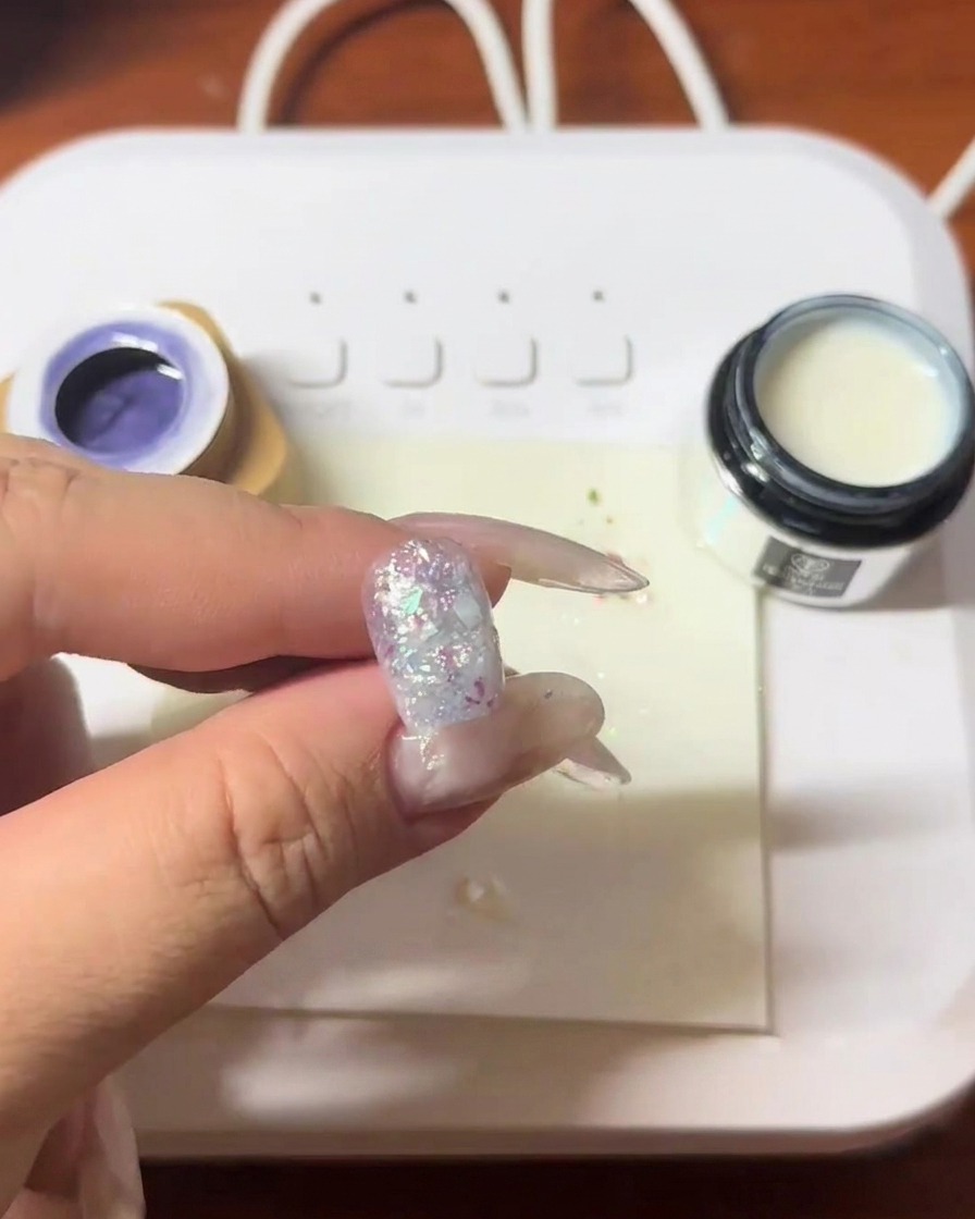 Un ongle avec des fragments de coquillages incrustés étant catalysé sous une lampe LED.
